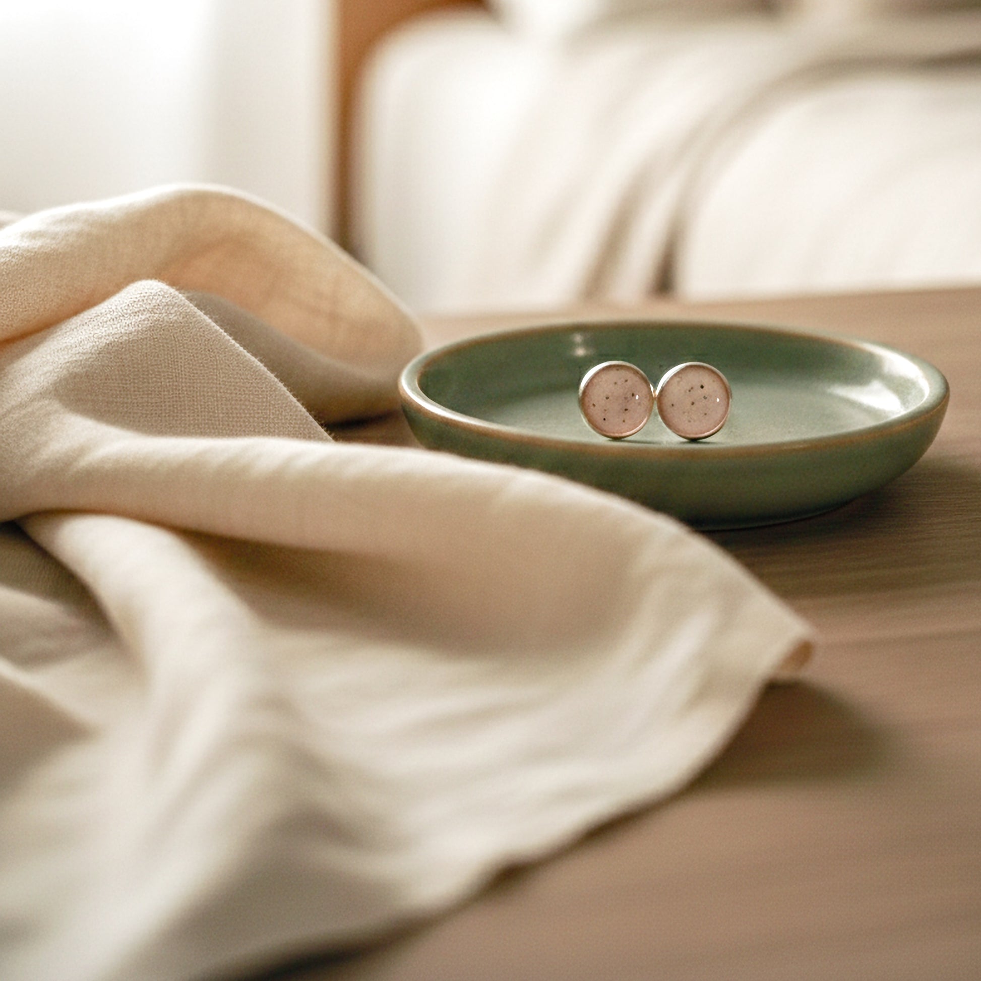 Pair of earrings on a green dish with a beige cloth in the background