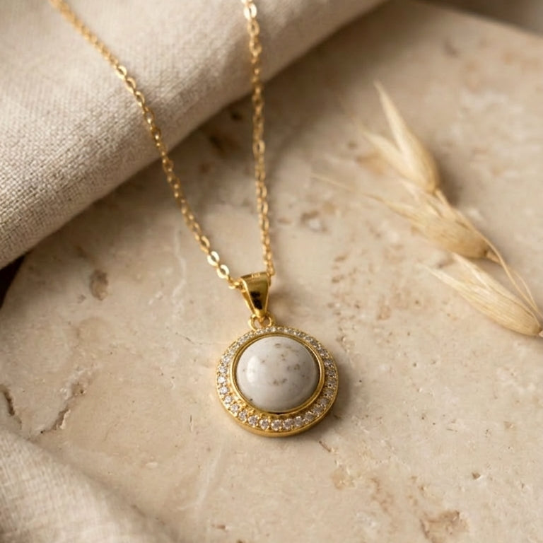 gold necklace with a round pendant on a stone surface
