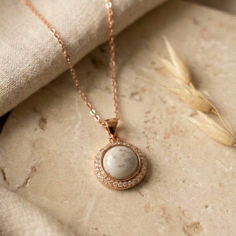 Rose gold necklace with a round pendant on a stone surface