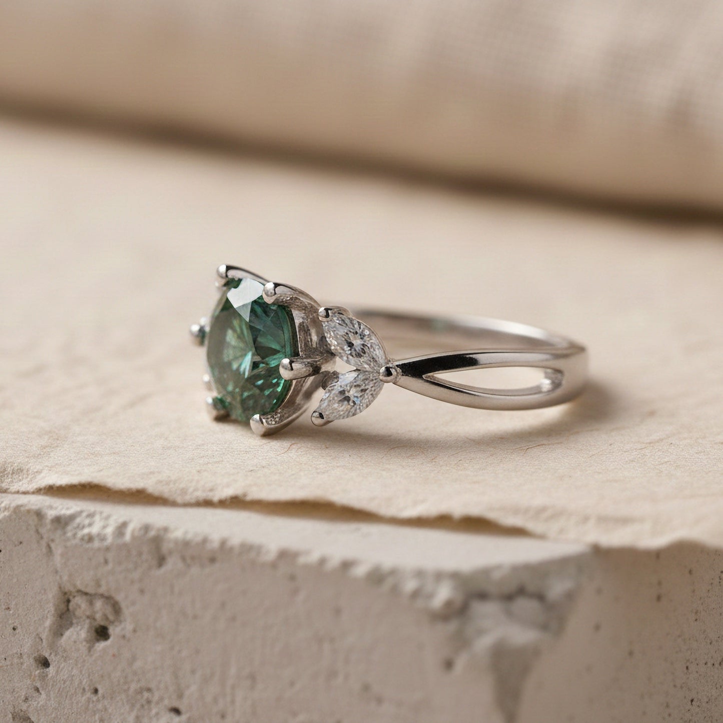 Silver ring with a blue-green moissanite gemstone on a textured surface