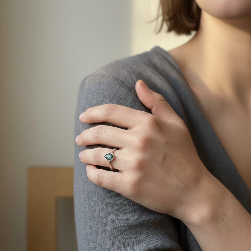 Person wearing a gray sweater with a ring on their finger, blurred background