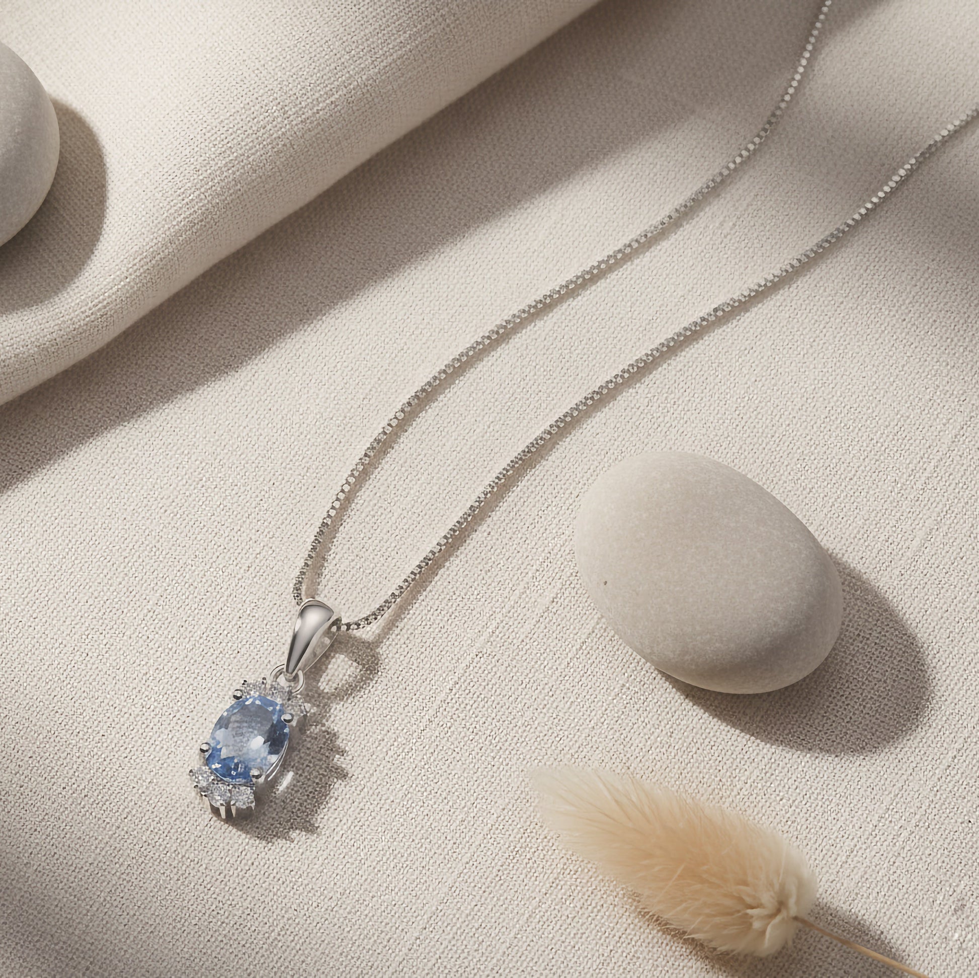 Silver necklace with a sky blue topaz gemstone pendant on a beige fabric background