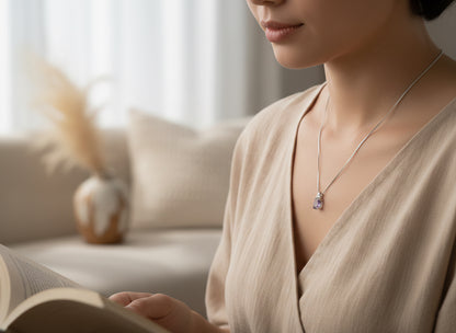 Woman wearing pendant with purple stone and a beige top while reading a book with a blurred background