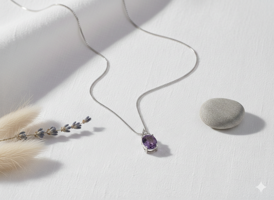 Necklace with a purple gemstone pendant on a white surface with a stone and dried plant.